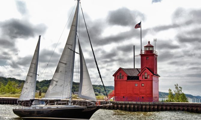 Sailboat sailing past a red lighthouse in Holland, Michigan.