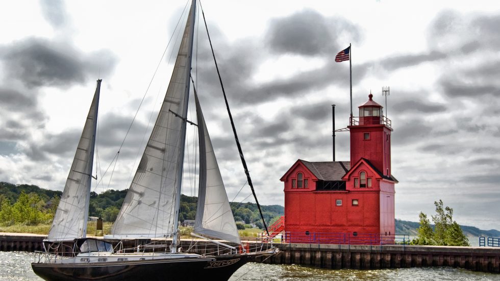 Sailboat sailing past a red lighthouse in Holland, Michigan.